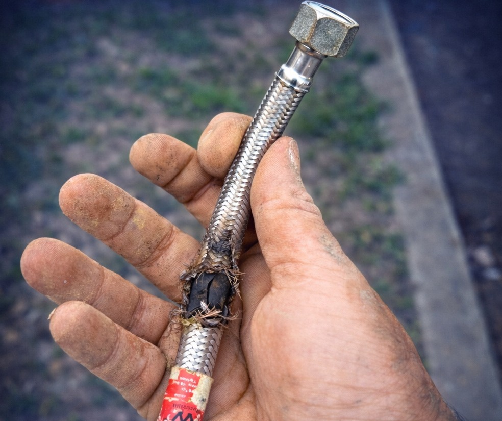 Close-up of a burst braided water hose fitting held in a tradesperson's hand