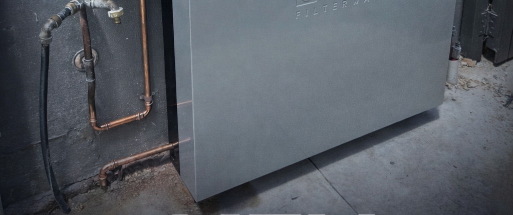 Whole-house water filtration unit installed on an exterior wall with copper pipework, an actual Meli Plumbing Services installation