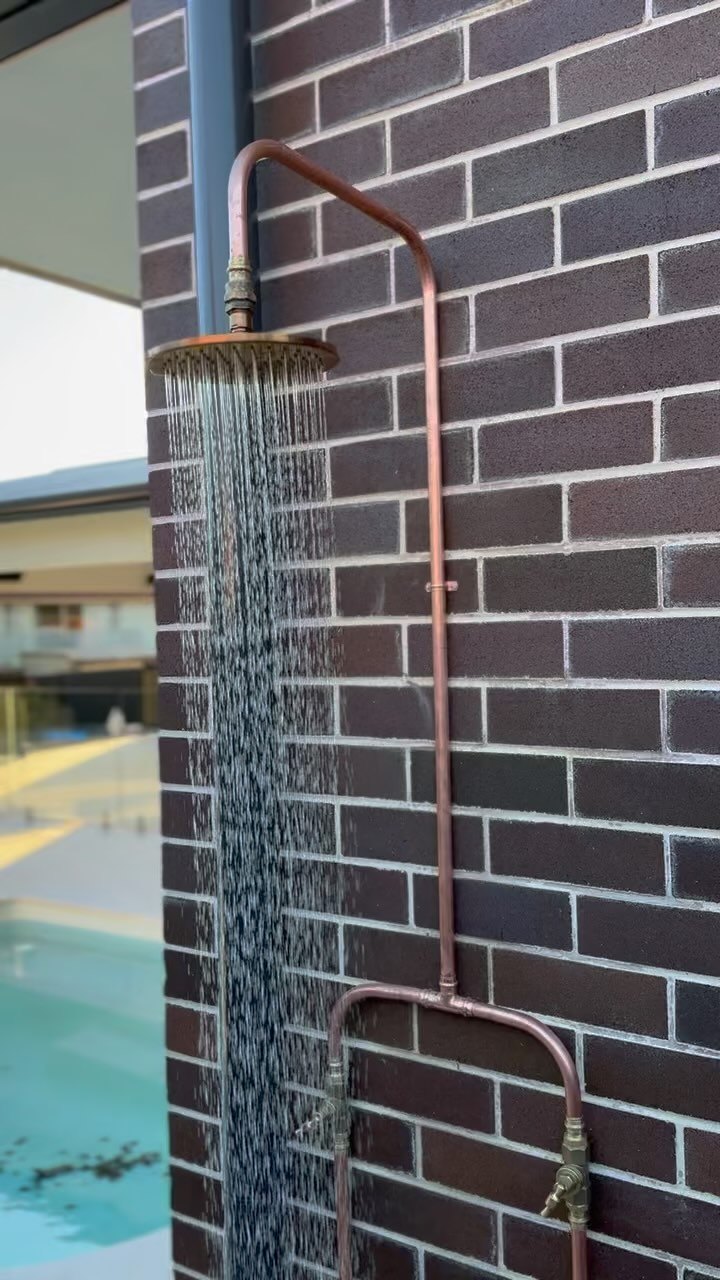 Outdoor copper shower installation against a brick wall beside a pool